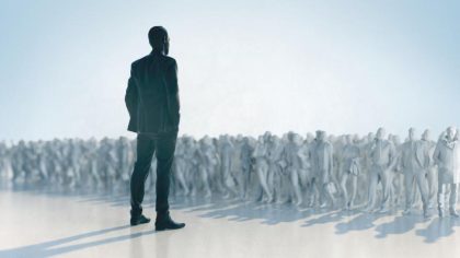 A suited man addresses a large crowd, conveying a message with enthusiasm and authority in a public speaking setting.